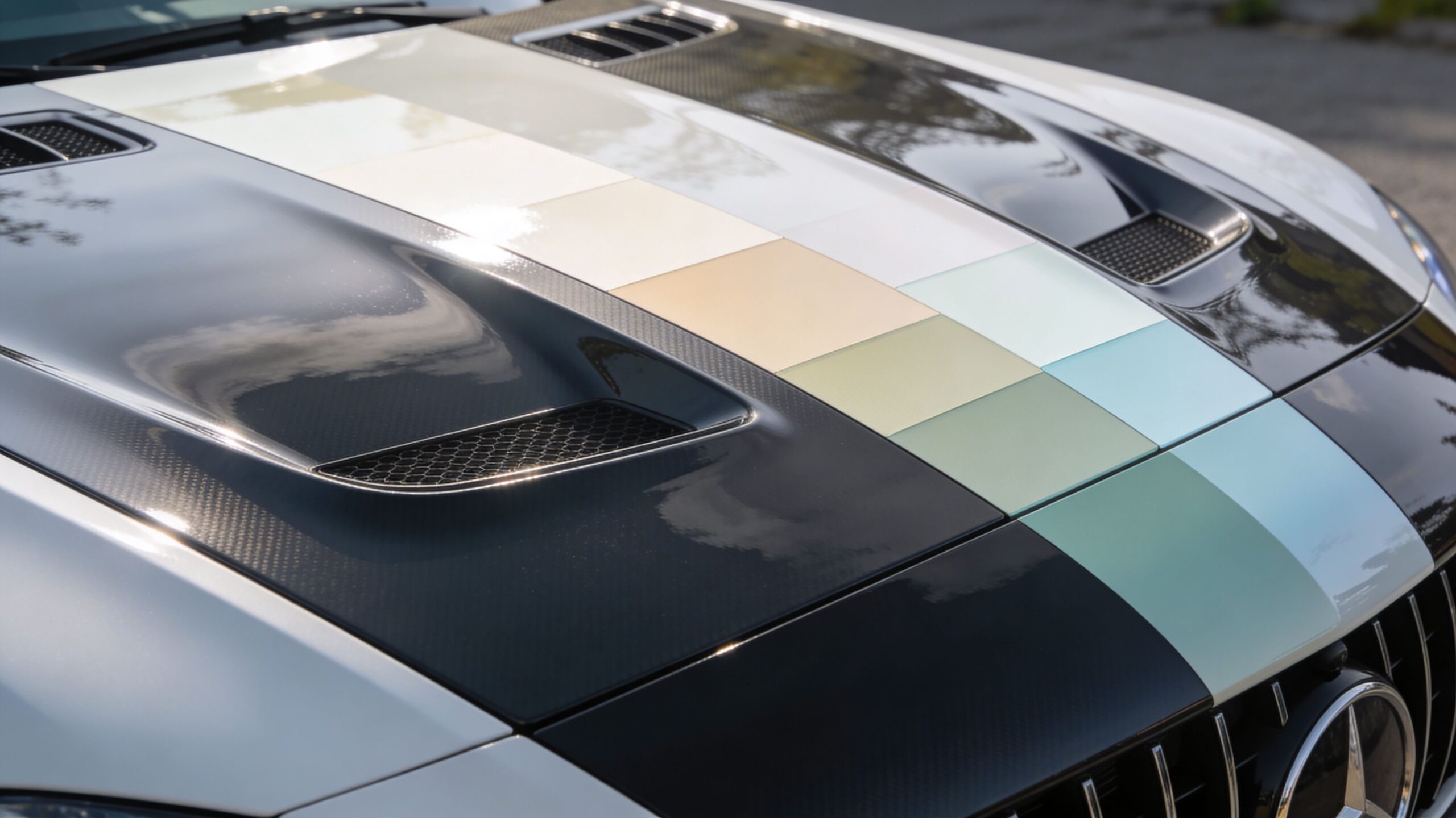 A close-up of a Mercedes-Benz car hood featuring a custom multi-colored stripe and carbon fiber details.