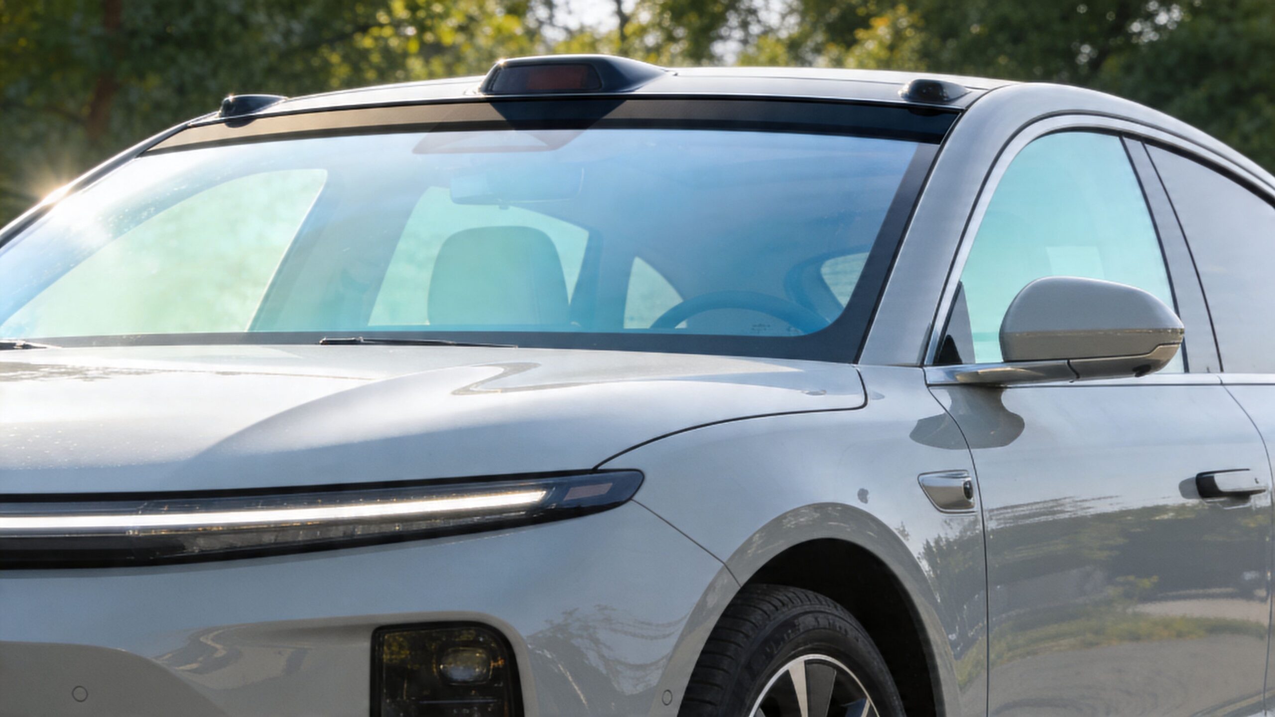 A close-up view of a modern gray car featuring a tinted front windshield and roof-mounted sensor pods.
