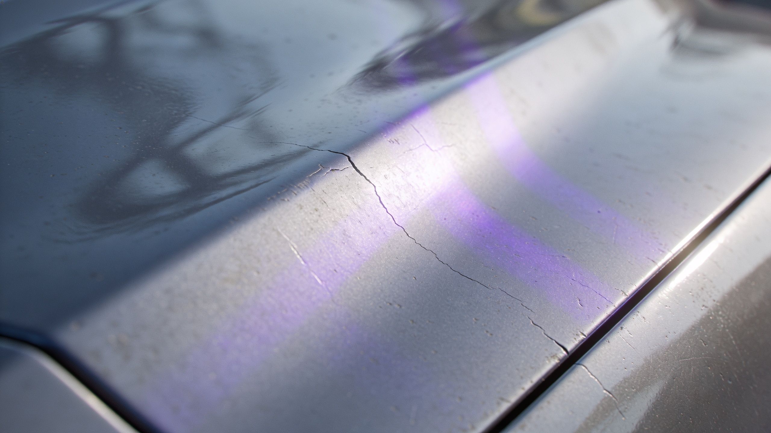 Close-up of a damaged car hood showing severe paint cracking and degradation with purple vinyl decal.