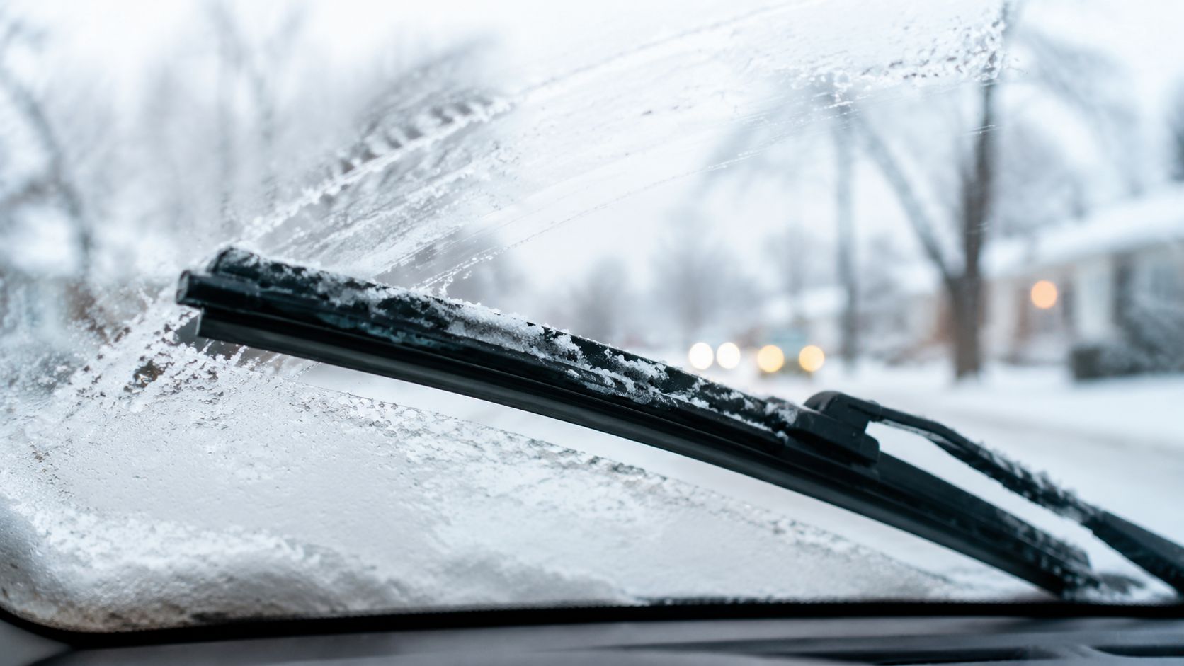 A car windshield wiper cleaning snow and ice off a frozen windshield during a winter storm.
