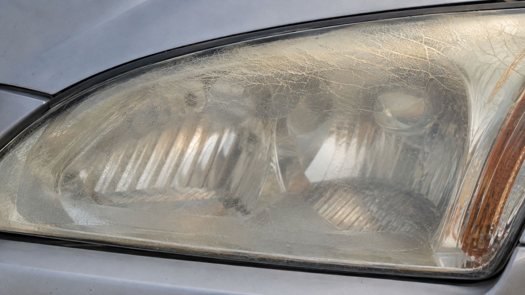 A close-up view of a car headlight showing severe oxidation and fine cracks on the plastic lens.